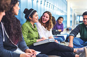 teenage girls sitting in front of the lockers laughing 